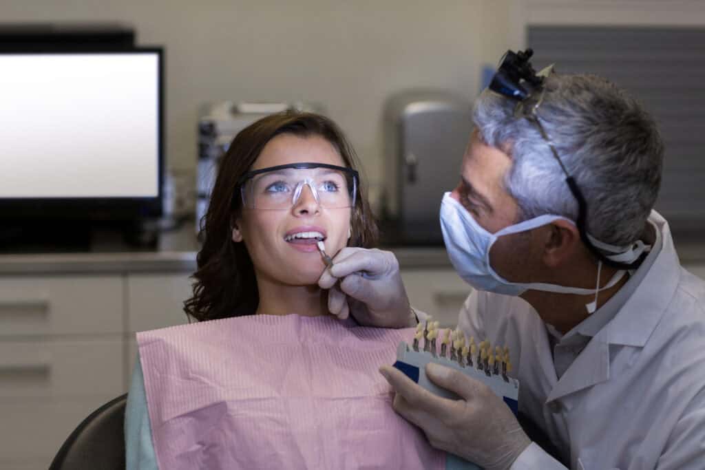 Dentist comparing tooth shades with a patient before placing a dental crown during a restorative dental consultation.